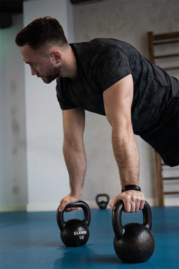 Mężczyzna ćwiczący w podporze na kettlebells w klubie Quantum Fitness